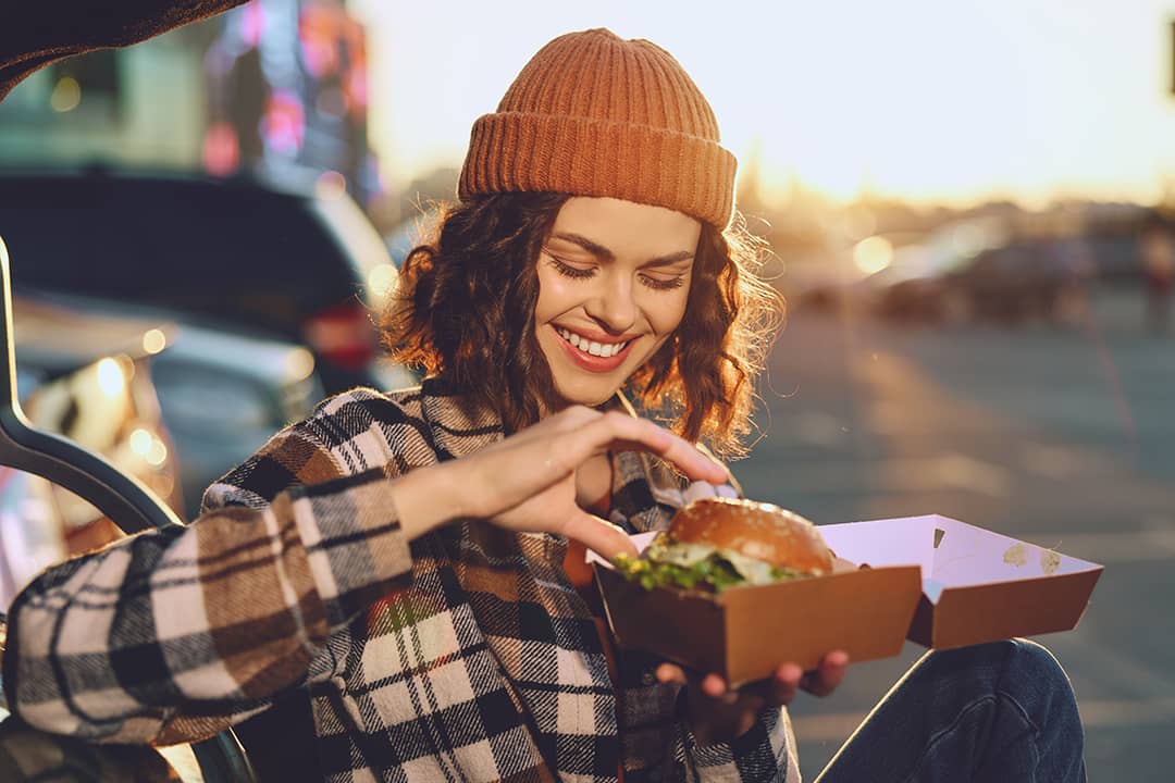 A young woman happily eating a takeout burger.